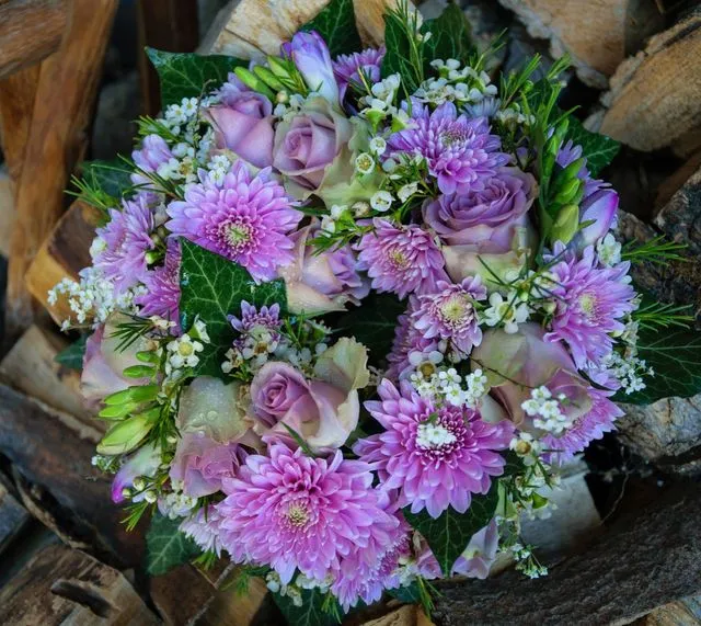 Runder Trauerstrauß mit violetten Chrysanthemen, Rosen und grünem Blattwerk