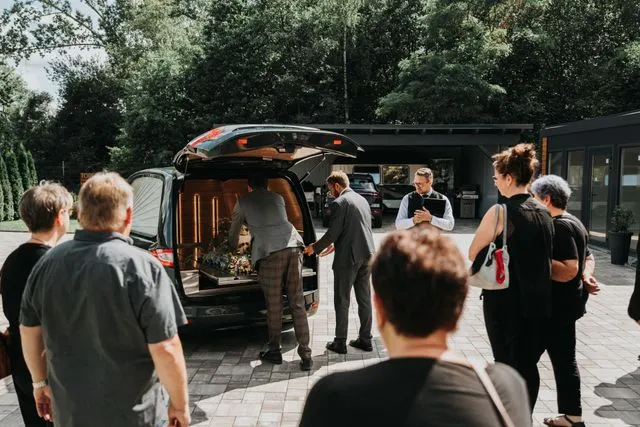 Trauergemeinde begleitet die Verladung des Sarges in ein Bestattungsfahrzeug vor dem Bestattungshaus