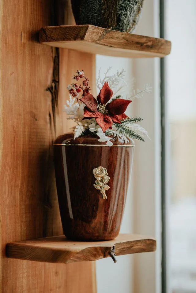 Holzurne mit floraler Dekoration auf einem Wandregal im Innenraum des Bestattungshauses Paul & Baar