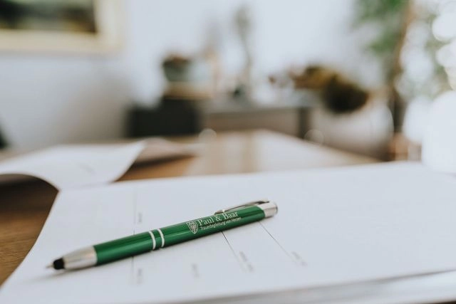 Kugelschreiber mit Logo des Bestattungshauses Paul & Baar liegt auf Formularen im Büro